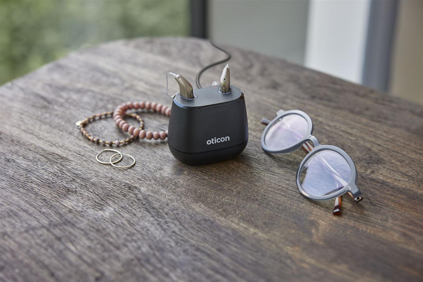 Oticon Intent mit Ladestation auf Tisch mit Brille und Armband